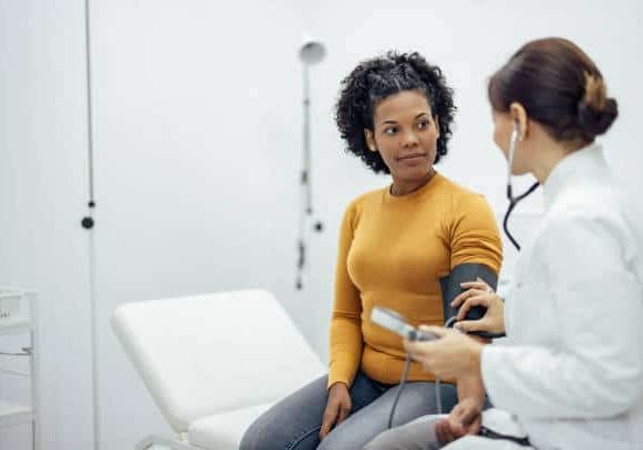 Doctor measuring blood pressure to a smiling woman as a part of a medical exam.